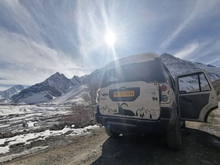 A Mahindra Scorpio car standing against snowy backdrop of Sagnam village of Pin valley