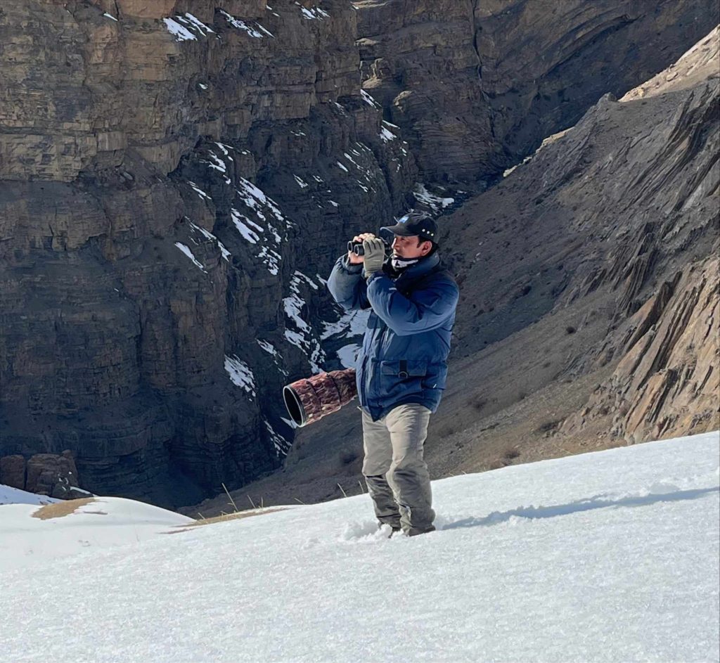 Gompo spotting wildlife using binocular on a snowy slope in Spiti valley